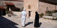 Eine Nonne und ein Mensch in Schutzanzug gehen über den Innenhof eines Klosters