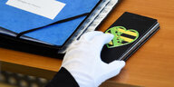 Ein Abgeordneter im Landtag von Sachsen greift mit einem Handschuh bekleidet nach seinem Telefon.