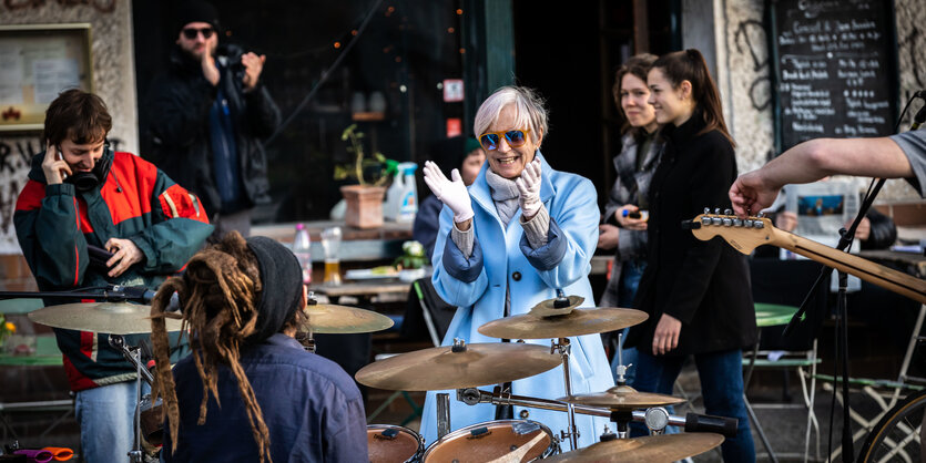 Eine Frau mit Handschuhen applaudiert Musikern während eines Konzerts am Senefelder Platz