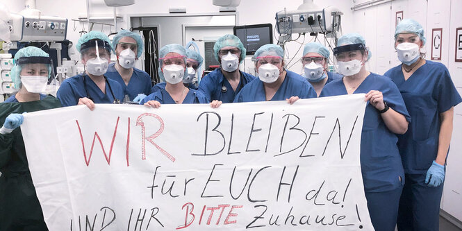 Team der Uni Klinik Essen halten einBanner hoch, auf dem geschrieben steht: Wir bleiben für euch da! Und ihr bitte zu Hause!