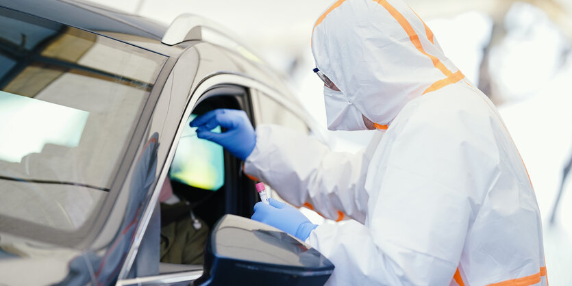 Person im Schutzanzug fasst in ein Autofenster