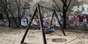 Eine Schaukel auf einem Spielplatz ist mit Absperrband gesperrt.