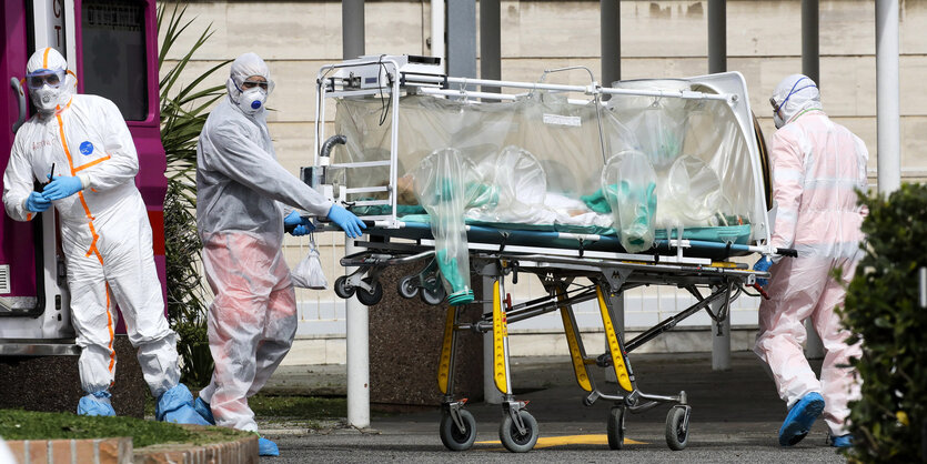 Medizinisches Personal schiebt ein Bett aus einer Intersivstation aus einem Krankenwagen.