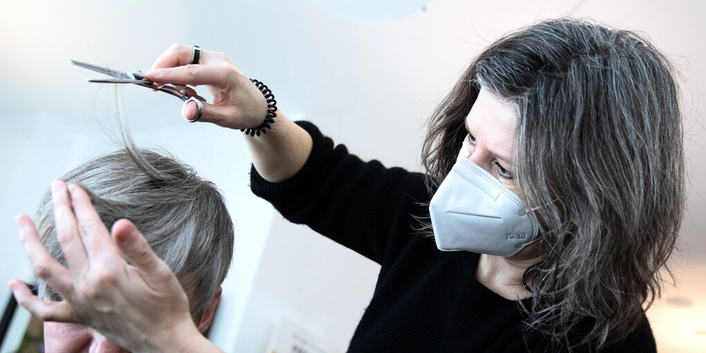 Eine Friseurin mit Mundschutz schneidet einer Kundin die Haare