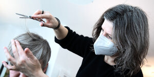 Eine Friseurin mit Mundschutz schneidet einer Kundin die Haare
