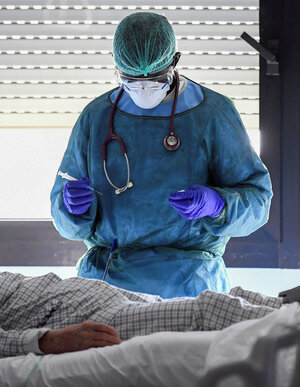 Ein Mediziner in blauer Schutzkleidung, Schutzbrille und Atemmaske hält eine Spritze in der Hand Ein Mediziner in blauer Schutzkleidung, Schutzbrille und Atemmaske hält eine Spritze in der Hand