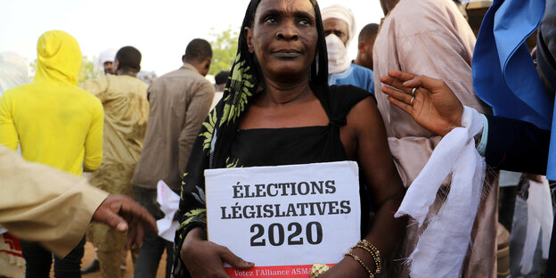 Eine Frau steht mit einem Wahlplakat bei einer Kundgebung in Mali.