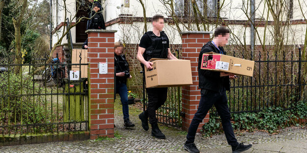 Zivilpolizisten tragen nach einer Razzia Kisten aus einem Haus.