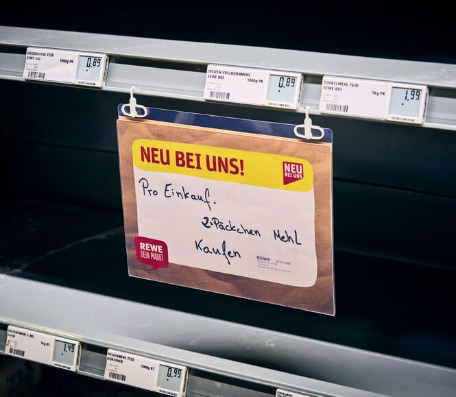 In einem leeren Supermarktregal hängt ein Schild: Pro Einkauf. 2 Päckchen Mehl kaufen