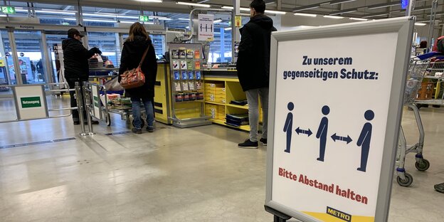 Ein Schuld in einem Berliner Großmarkt biettet die Kunden, in Corona-Zeiten genug Abstand beim Anstehen zu halten