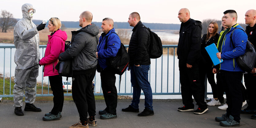 Menschen stehen in einer Schlange, bei der ersten Person wird Fieber gemessen.