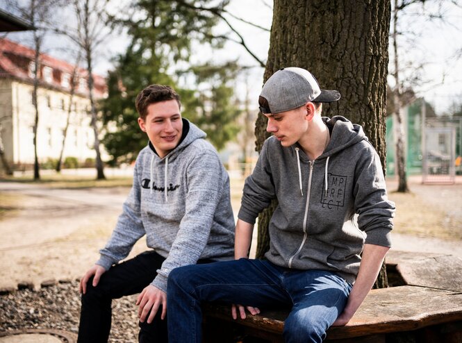 Maurice Heilmann und Felix Jahnke vom Jugendbeirat Grünheide sitzen auf einer Bank vor einem Baum