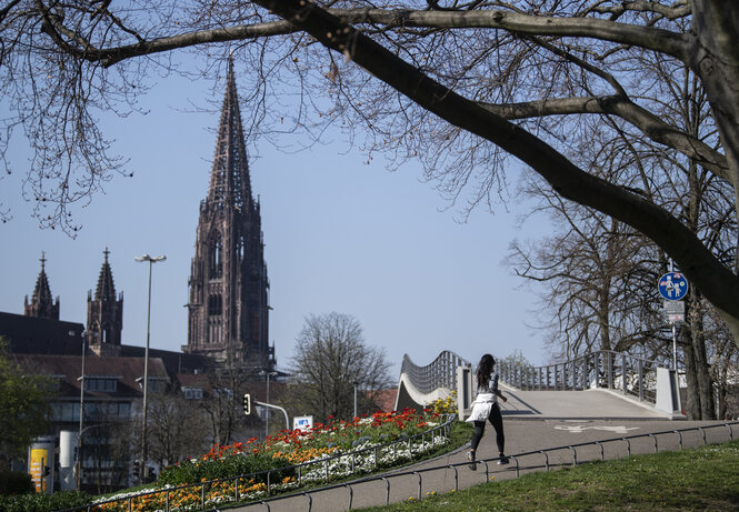 Ein Joggerin läuft im Stadtpark vor der Kulisse des Freiburger Münsters.