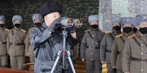 Kim Jong Un steht an einem Fernglas, Soldaten mit Mundschutz im Hintergrund.