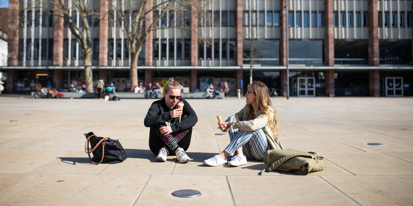 zwei frauen sitzen auf einem Platz und essen ein Eis