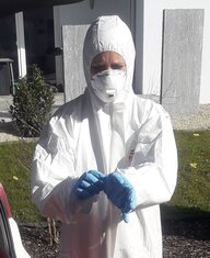 Eine Ärztin trägt einen weißen Schutzanzug und blaue Handschuhe