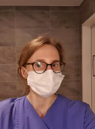 Eine junge Frau in Krankenhauskleidung mit Mundschutz und Brille