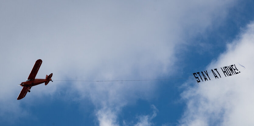 Flugzeug in der Luft mit Banner "Stay at home"