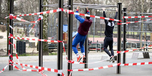 Zwei Männer an mit Absperrband gesperrten Fitnessgeräten.