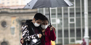 Ein Paar mit Mundschutz unter einem Regenschirm