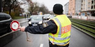 Ein Polizist steht mit einer Kelle auf einer Straße.