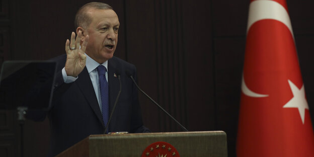 Der türkische Präsident Erdogan mit erhobener Hand neben der staatlichen Flagge