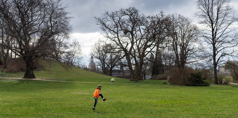 Ein einsames Kind kickt einen Ball über eine Wiese.