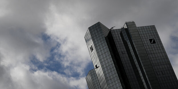 Sonnenlicht fällt bei trübem Wetter auf die Fassade und das Logo der Deutschen Bank-Zentrale im Frankfurter Bankenviertel.