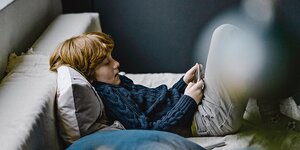 Junge sitzt mit Smartphones in der Hand auf Bett