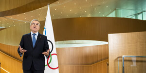 ein Mann steht vor einer olympischen Fahne und spricht