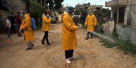Menschen in gelbem Schutzanzügen desinfizieren eine Strasse