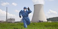 Mann inSchutzkleidung rennt vor Atomkraftwerk auf einer Wiese