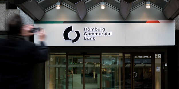 Das gläserne Eingangsportal der Hamburg Commercial Bank mit gezacktem Vordach wird von einem Mann fotografiert