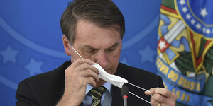 Brasiliens Präsident Bolsonaro setzt eine Atemschutzmaske auf