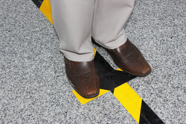 Die Füße einer Person stehen parallel zueinander, dazwischen verläuft ein schwarz-gelber Warnstreifen