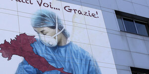Malerei an einer Hauswand: Eine Frau mit Mundschutz und im blauen Kitte umarmt Italien