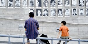 Ein Mann und ein Kind sitzen vor schwarzweis Bilder der Decaparesidcos unter Pinochet