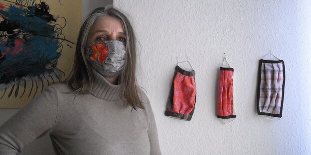 Eine Frau mit Atemmaske, neben ihr hängen drei weitere Masken an der Wand