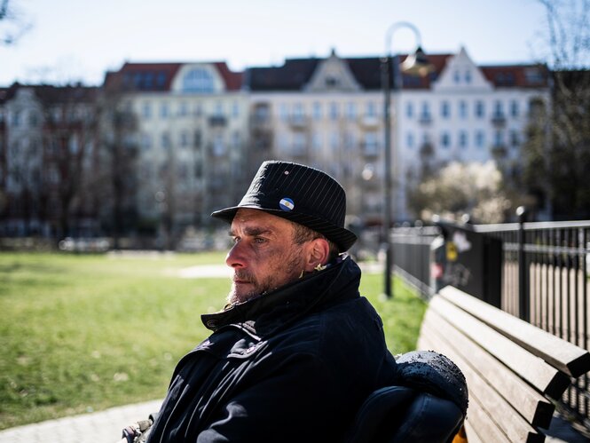 Ein Mann mit Hut sitzt auf einer Parkbank.