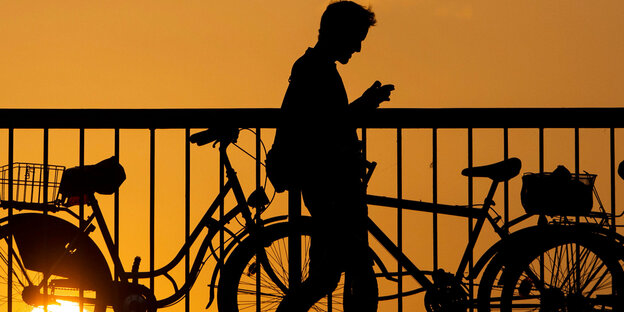 Ein junger Mann blickt auf sein Handy, während er ei Sonnenuntergang über die Jannowitzbrücke geht.