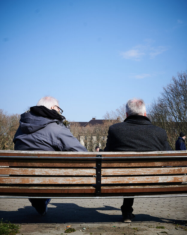 Corona in Berlin: Zwei Männer sind von hinten zu sehen, wie sie bei schönem Wetter auf einer Parkbank sitzen Corona in Berlin: Zwei Männer sind von hinten zu sehen, wie sie bei schönem Wetter auf einer Parkbank sitzen