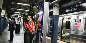 Ein Mann mit Schal vor dem Mund an einer U-Bahnhaltestelle