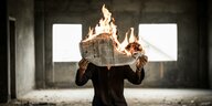 Eine Person hält eine brennende Zeitung vor dem Gesicht
