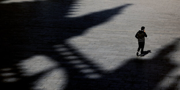 Von erhöhter Position aufgenommen: Ein Mann geht über den leeren Kölner Bahnhofsplatz. Man sieht ihn zwischen den Schatten des Doms.