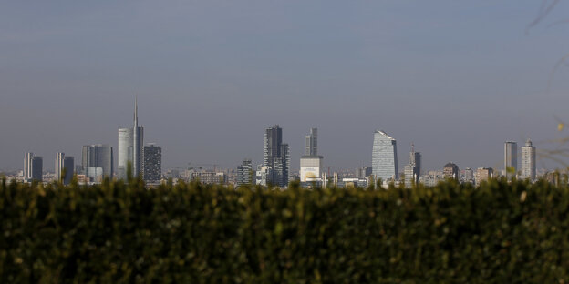 Hinter einer Hecke sieht man die Skyline von Mailand