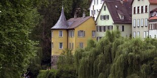 Ein gelbes Haus mit einem Turm-Anbau steht zwischen Bäumen