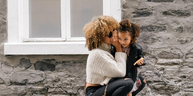 Eine Mutter flüstert ihrer kleinen Tochter etwas ins Ohr