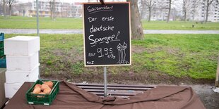 Eine Kiste mit Süßkartoffeln steht auf einem Wochenmarkt unter einem Schild mit der Aufschrift "Der erste deutsche Spargel". Um die Ausbreitung des Coronavirus zu verlangsamen hat Sachsen auch Wochenmärkte schließen lassen.