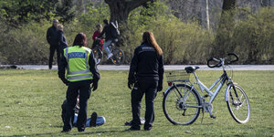 Polizisten stehen vor einem mann, der im Park sitzt