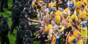 Gelb-blaue Braunschweig-Fans stehen schwarz gekleideeten, behelmten Polizisten gegenüber